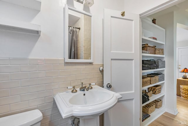 bathroom with a shower with curtain, wood-type flooring, sink, tile walls, and toilet