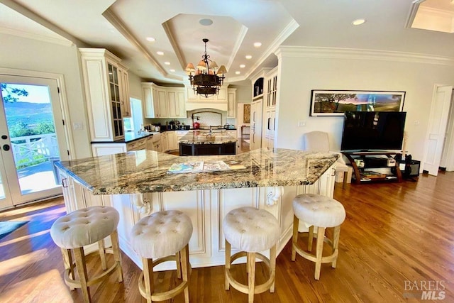 kitchen featuring a raised ceiling, hanging light fixtures, cream cabinets, a large island with sink, and dark hardwood / wood-style flooring