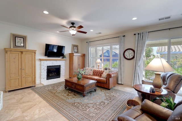 living room featuring ornamental molding, a stone fireplace, and ceiling fan