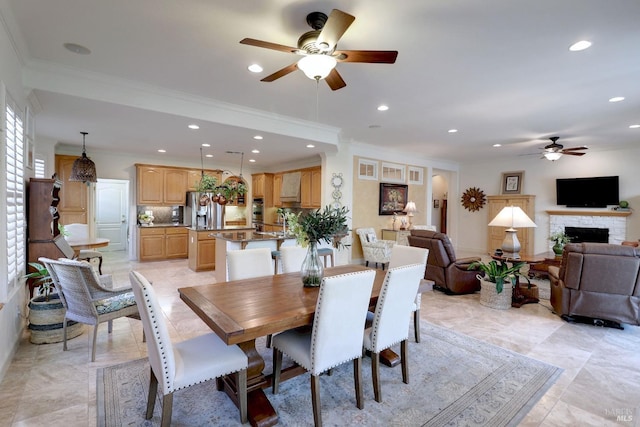 dining space featuring ceiling fan, a stone fireplace, and crown molding