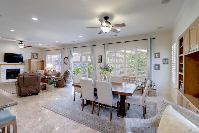 dining area featuring ceiling fan, a stone fireplace, and ornamental molding