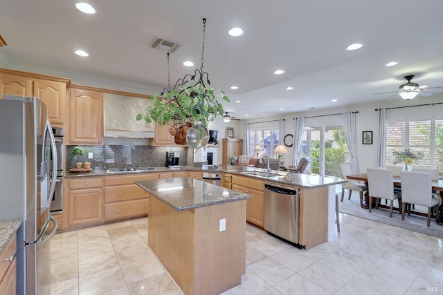 kitchen with light brown cabinets, appliances with stainless steel finishes, a kitchen island, and light stone counters