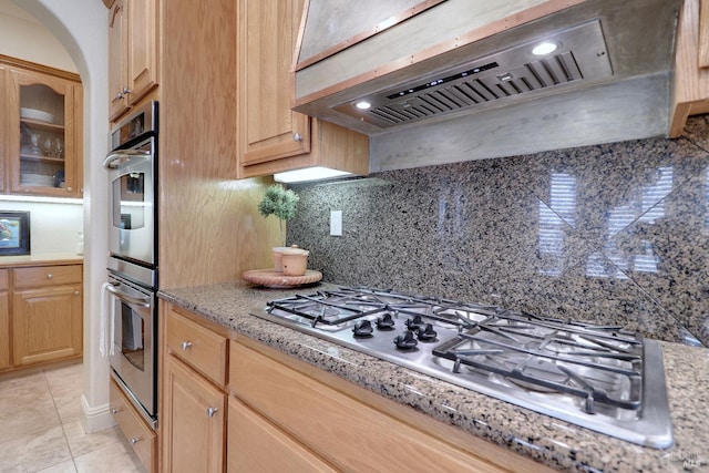 kitchen featuring custom exhaust hood, decorative backsplash, light tile patterned floors, light brown cabinetry, and stainless steel appliances