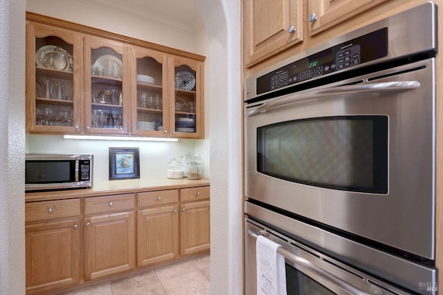 kitchen with appliances with stainless steel finishes, light tile patterned floors, and ornamental molding