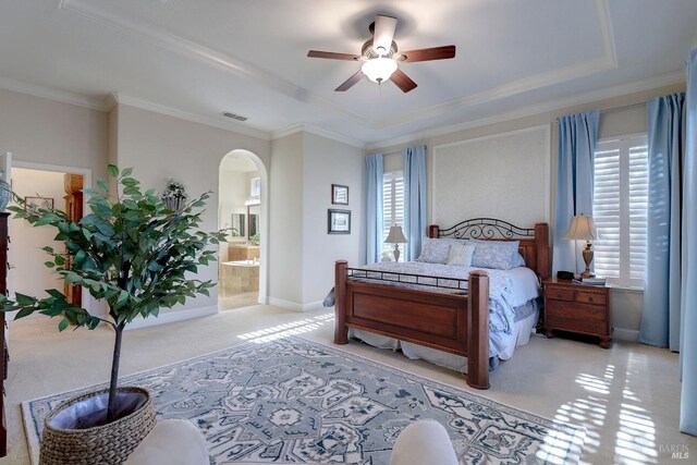 bedroom with ensuite bath, a tray ceiling, ceiling fan, ornamental molding, and light colored carpet