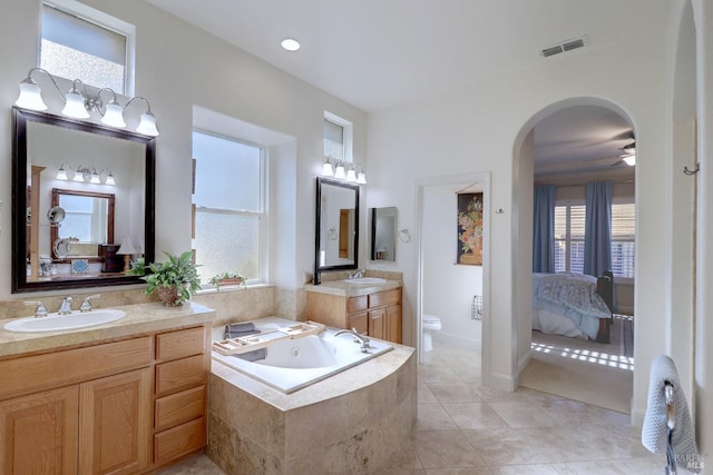 bathroom featuring tiled bath, toilet, ceiling fan, vanity, and tile patterned flooring