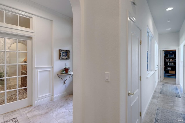 hall featuring baseboards, visible vents, arched walkways, crown molding, and recessed lighting