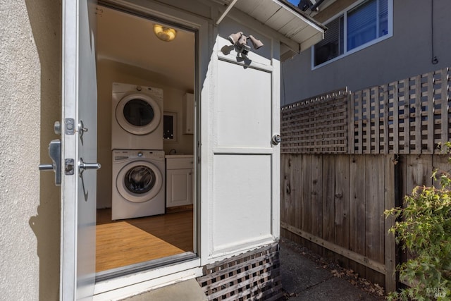 laundry area with wood-type flooring, cabinets, wooden walls, and stacked washer / dryer