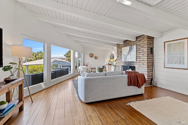 living room with hardwood / wood-style flooring, beam ceiling, a brick fireplace, and wood walls