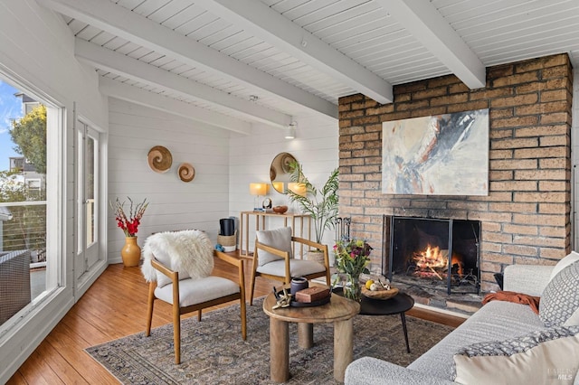 living room with hardwood / wood-style flooring, a brick fireplace, beam ceiling, and wood walls