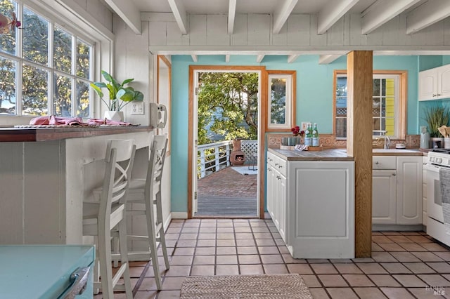 kitchen with white cabinetry, white gas range, light tile patterned flooring, and beamed ceiling