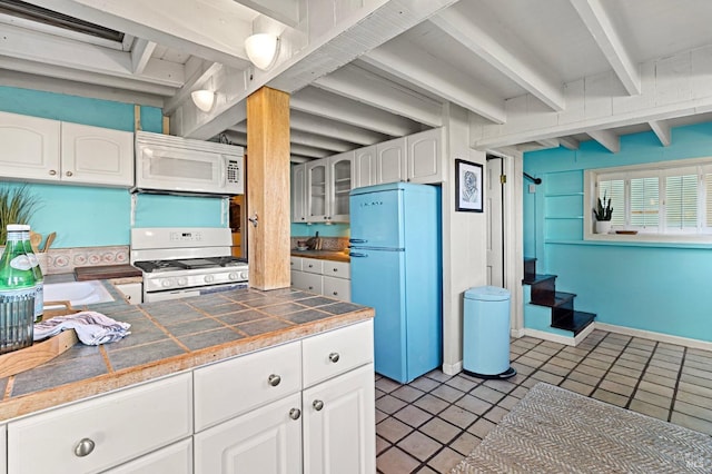 kitchen with light tile patterned flooring, white cabinets, tile counters, white appliances, and beam ceiling