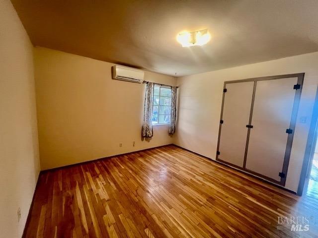 unfurnished bedroom featuring a wall unit AC, wood-type flooring, and a closet