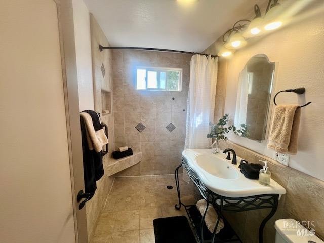 bathroom with toilet, walk in shower, vanity, and tile walls