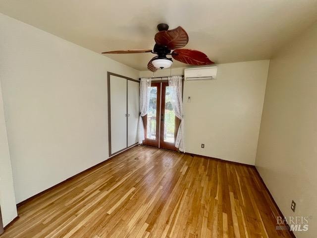 unfurnished bedroom with a wall mounted AC, ceiling fan, light wood-type flooring, a closet, and french doors