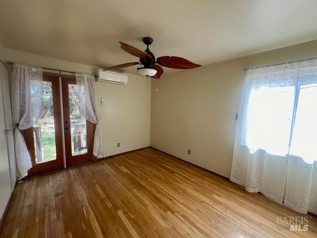 empty room featuring french doors, light hardwood / wood-style floors, a wall mounted AC, and ceiling fan