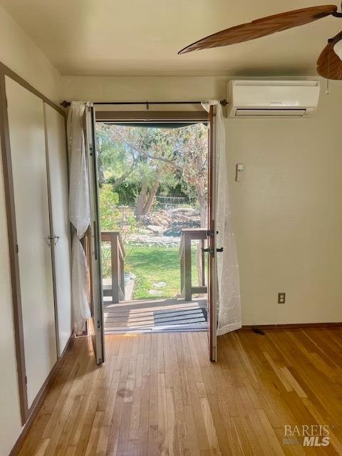 doorway with a wall mounted air conditioner, light wood-type flooring, and ceiling fan