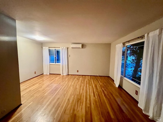 unfurnished room featuring a wall mounted AC and hardwood / wood-style flooring