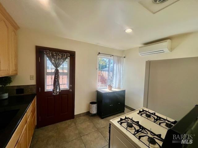 kitchen with a wall mounted air conditioner, light brown cabinets, white gas range oven, and light tile patterned floors