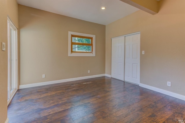 unfurnished bedroom with beamed ceiling, a closet, and dark hardwood / wood-style flooring