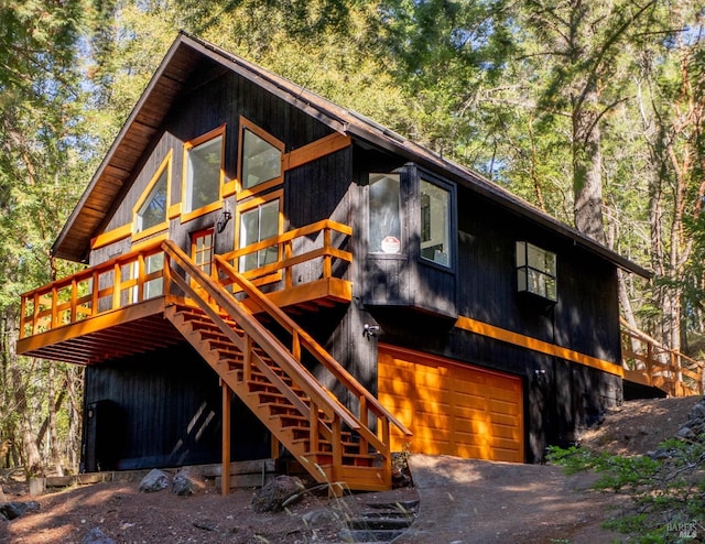 view of front facade featuring a view of trees, dirt driveway, stairway, a garage, and a deck