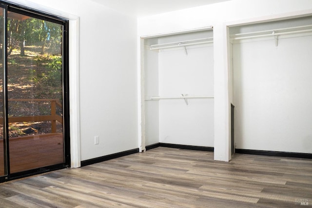 unfurnished bedroom with multiple closets, wood finished floors, and baseboards