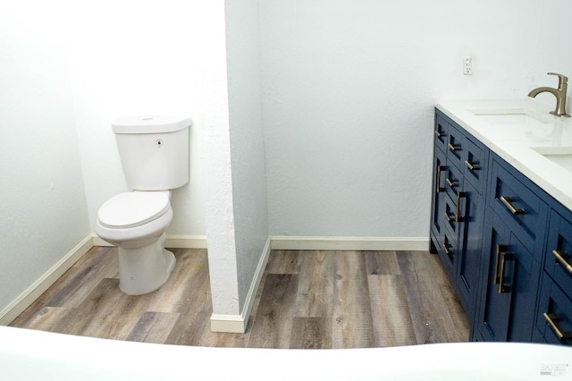 bathroom with toilet, wood finished floors, a sink, double vanity, and baseboards