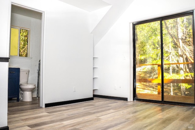 unfurnished bedroom featuring wood finished floors, ensuite bath, and baseboards
