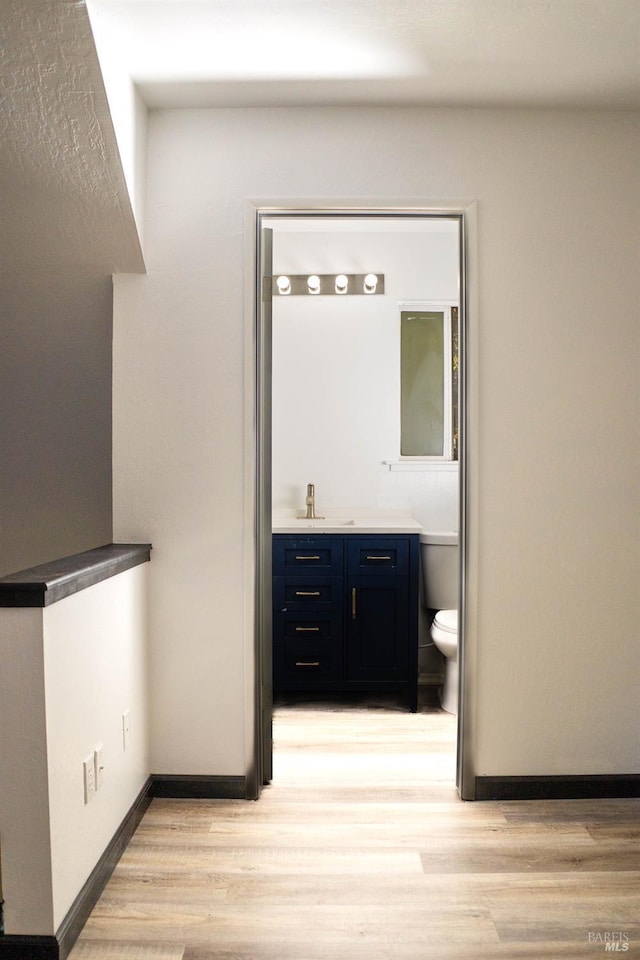 bathroom with toilet, vanity, wood finished floors, and baseboards
