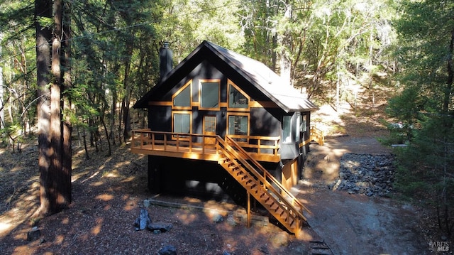 rear view of house featuring a view of trees, stairway, metal roof, and a wooden deck