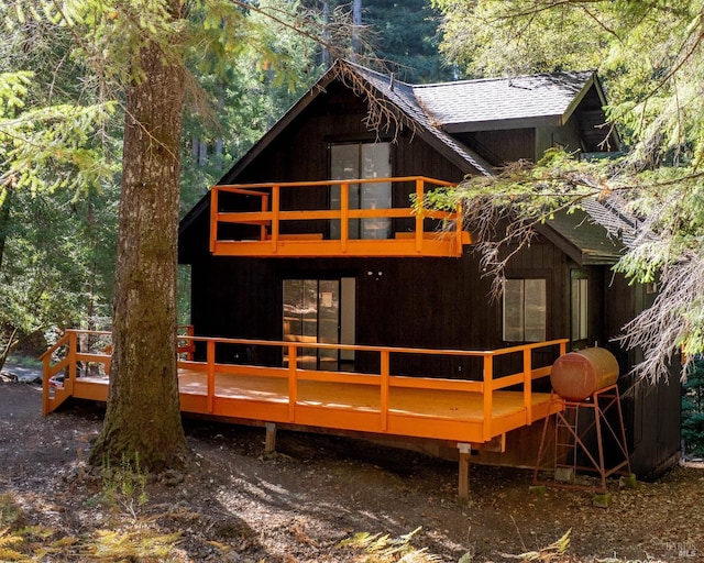 rear view of property featuring a wooded view, a balcony, a wooden deck, and a shingled roof