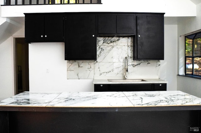 kitchen with a sink, backsplash, light countertops, and dark cabinets