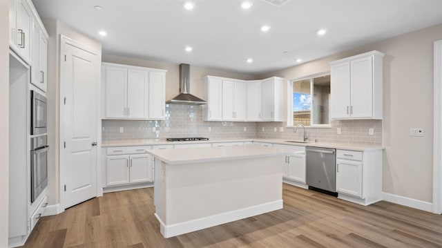 kitchen featuring light wood-style flooring, a sink, white cabinets, appliances with stainless steel finishes, and wall chimney range hood