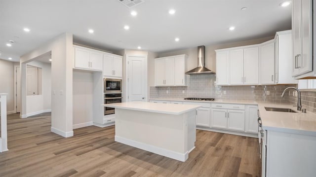 kitchen with visible vents, wall chimney range hood, built in microwave, stainless steel oven, and a sink