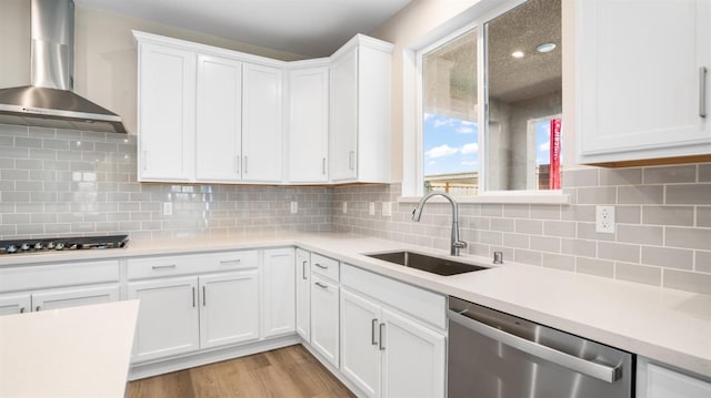 kitchen featuring light wood-type flooring, a sink, stainless steel appliances, wall chimney exhaust hood, and light countertops