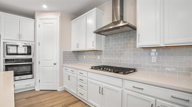 kitchen featuring light countertops, appliances with stainless steel finishes, wall chimney range hood, and white cabinets
