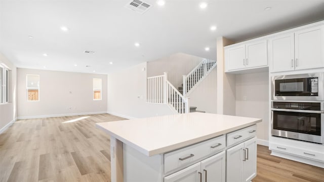 kitchen with light wood-style flooring, white cabinets, visible vents, built in microwave, and oven