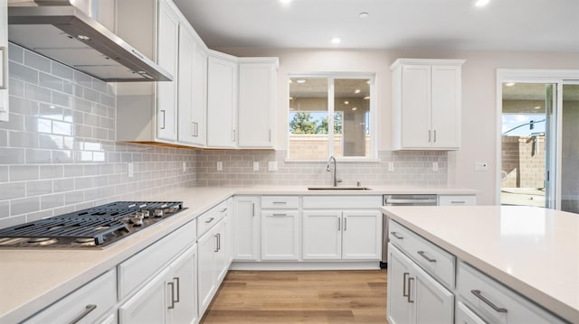 kitchen with white cabinetry, stainless steel appliances, wall chimney range hood, and a sink