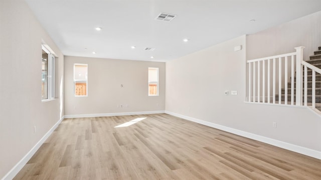 unfurnished room featuring light wood-type flooring, visible vents, baseboards, and stairs