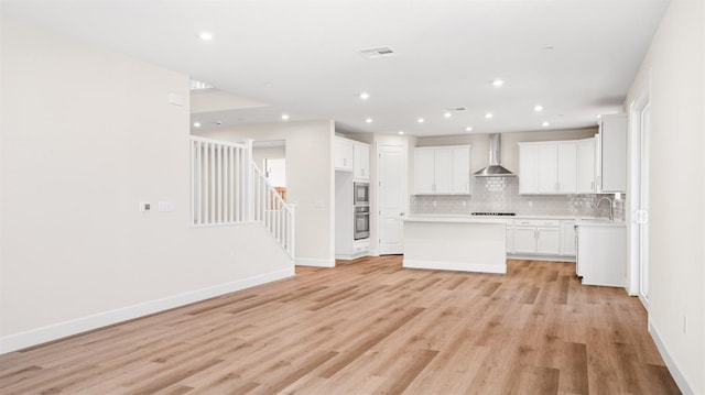 kitchen with stovetop, stainless steel oven, wall chimney exhaust hood, tasteful backsplash, and a center island