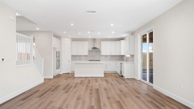 kitchen featuring a sink, a kitchen island, light wood-style floors, wall chimney exhaust hood, and decorative backsplash