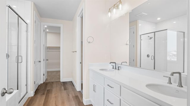 bathroom featuring wood finished floors, double vanity, a stall shower, a sink, and a walk in closet