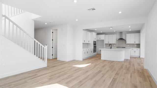 kitchen with white cabinetry, light countertops, wall chimney range hood, and light wood-style flooring