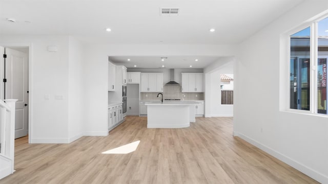 kitchen with visible vents, wall chimney range hood, backsplash, white cabinets, and light countertops