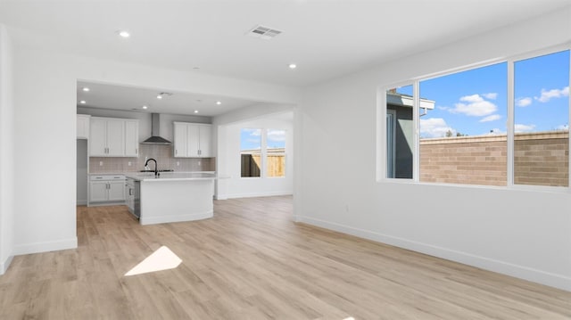 unfurnished living room with visible vents, baseboards, light wood-style floors, and a sink