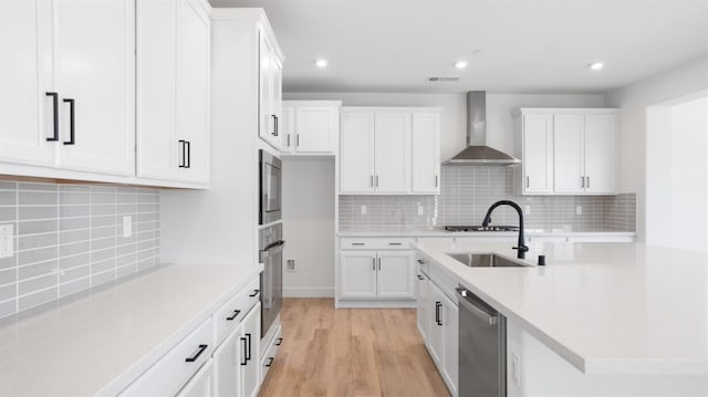 kitchen with light countertops, appliances with stainless steel finishes, white cabinets, wall chimney exhaust hood, and a sink