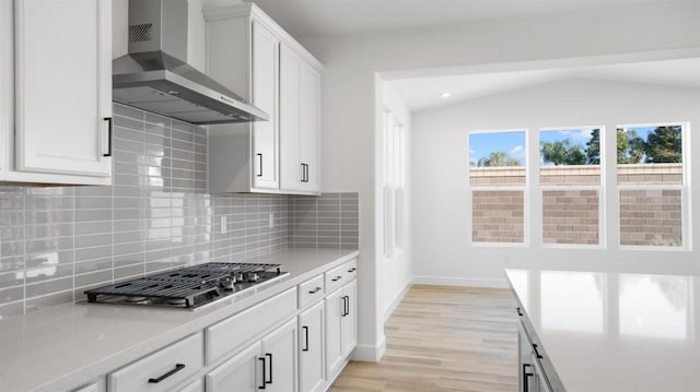 kitchen with lofted ceiling, stainless steel gas stovetop, wall chimney exhaust hood, and light countertops