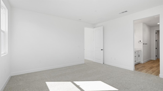 empty room with a wealth of natural light, visible vents, baseboards, and light colored carpet