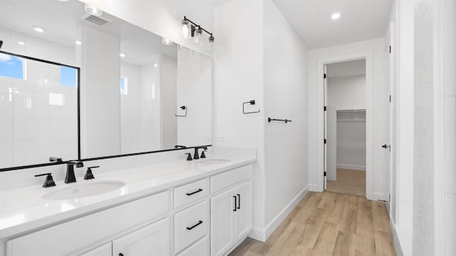 full bathroom featuring a tile shower, wood finished floors, a walk in closet, and a sink