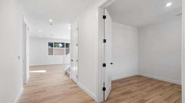 corridor with light wood-style floors, visible vents, and baseboards